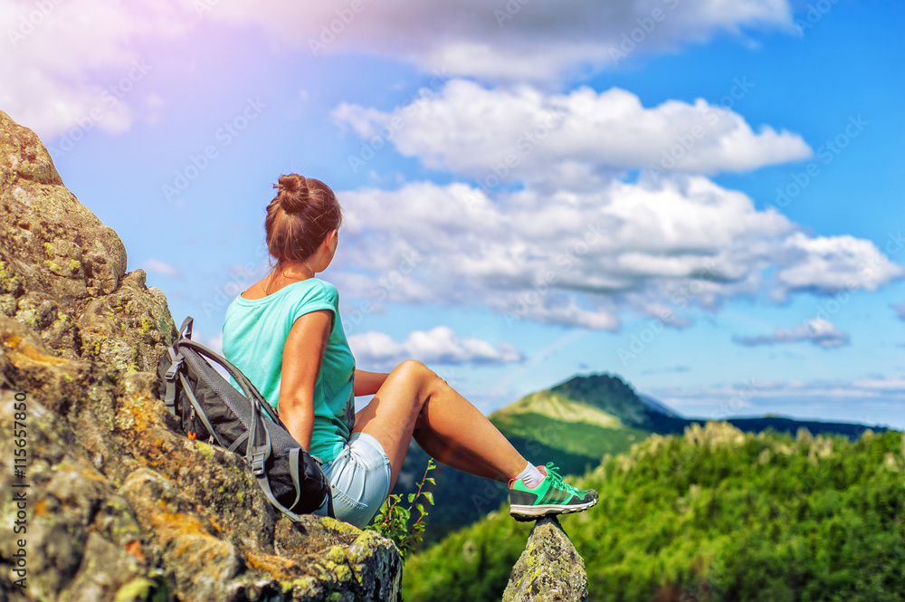 Young woman tourist sitting on the top of the mountain and enjoying amazing landscape