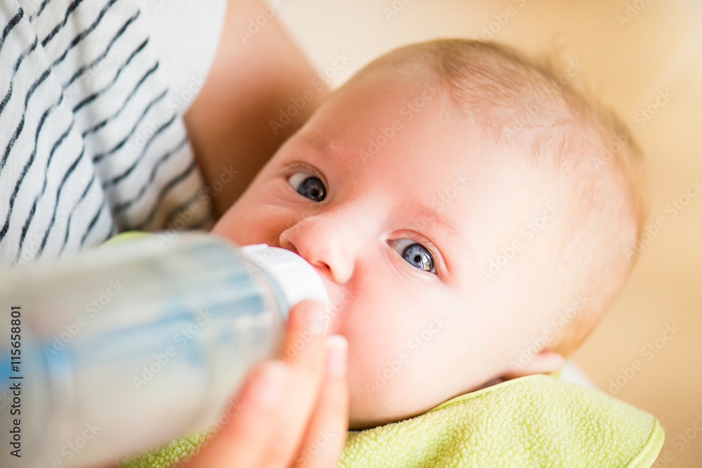 Unrecognizable mother feeding baby son, milk in bottle, close up Unrecognizable mother feeding baby son, milk in bottle, close up