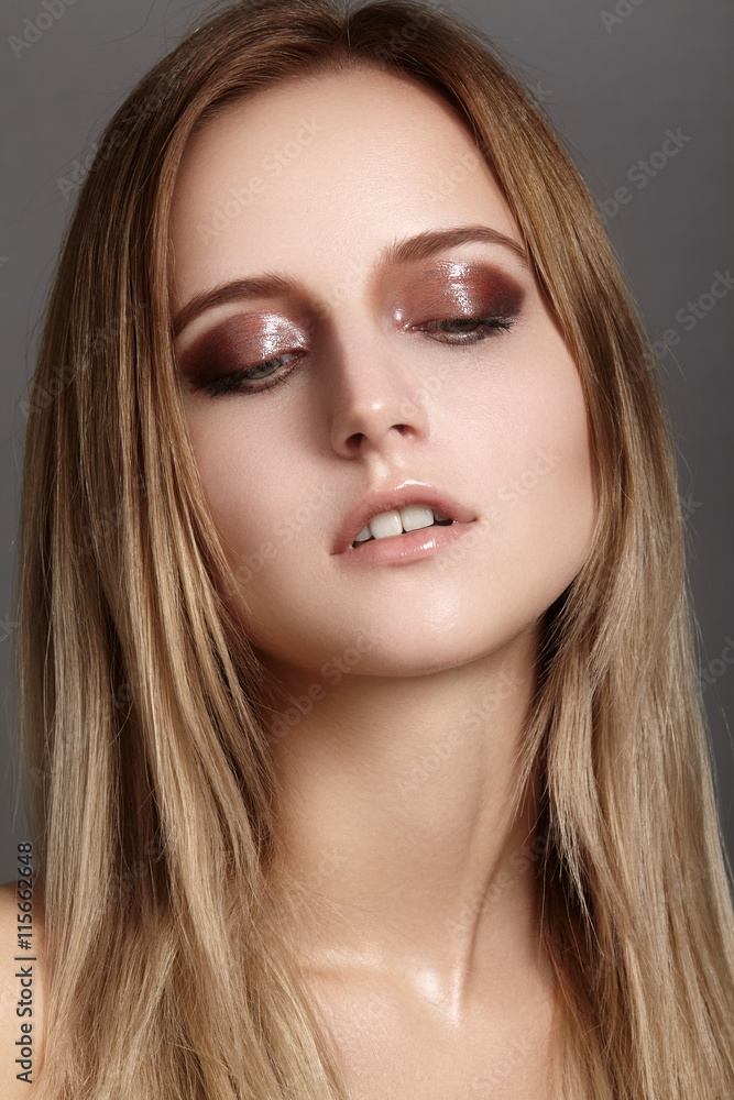 Naklejka premium Beautiful young woman with gloss eyes and lips visage, dark blond color long hair. Beauty portrait with clean skin, glamour fashion makeup. Cosmetics, make up, hairstyle. Haircare