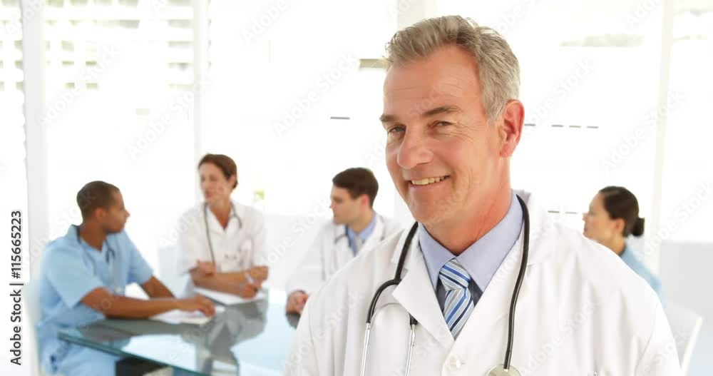 Happy doctor looking at camera and his staff behind him Happy doctor looking at camera and his staff behind him
