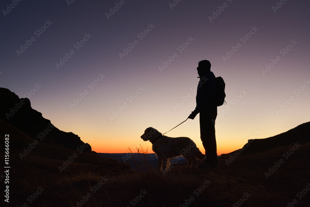 Silhouette of hiker with small backpack and his dog at sunrise