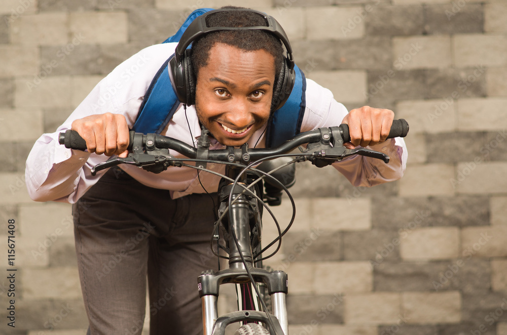 Man wearing grey office pants, white red business shirt and backpack standing by bicycle in racing position smiling, brick wall background Man wearing grey office pants, white red business shirt and backpack standing by bicycle in racing position smiling, brick wall background