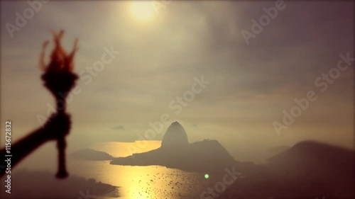 Hand of torchbearer athlete holding sport torch in silhouette against Rio de Janeiro, Brazil sunrise skyline in selective focus against Sugarloaf Mountain photo