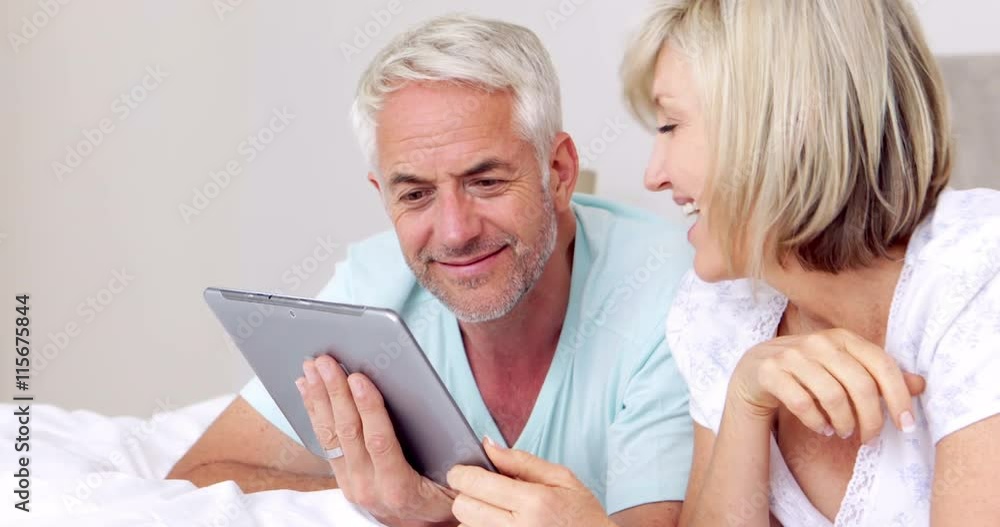 Happy couple lying on bed using tablet together Happy couple lying on bed using tablet together