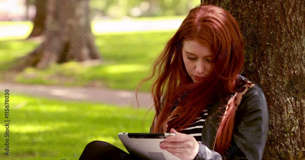 Pretty redhead using tablet pc in the park on a sunny day Pretty redhead using tablet pc in the park on a sunny day