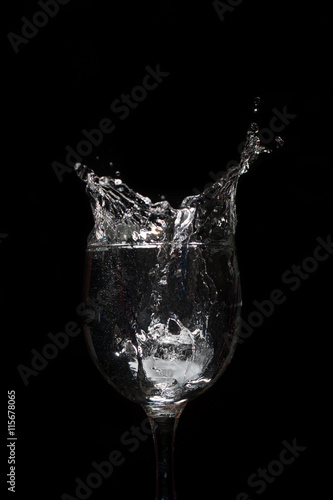Water splash with ice in glass on black