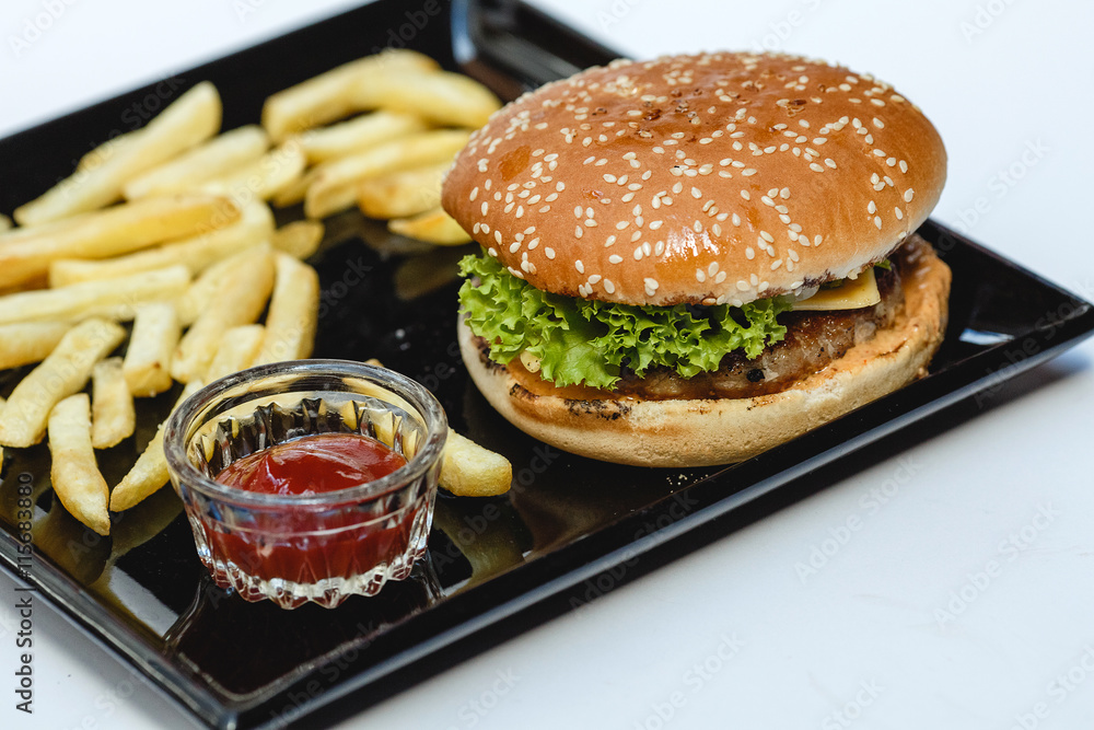 Hamburger and french fries on black plate on white background