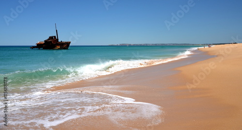 Horizontal landscape of the beach with a fisherman, shipwreck in the background on a sunny day (Stockton Beach, NSW, Australia)