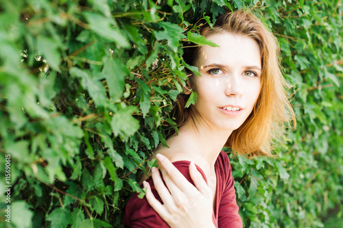 girl in a dress gently touches the hand green bush leaves