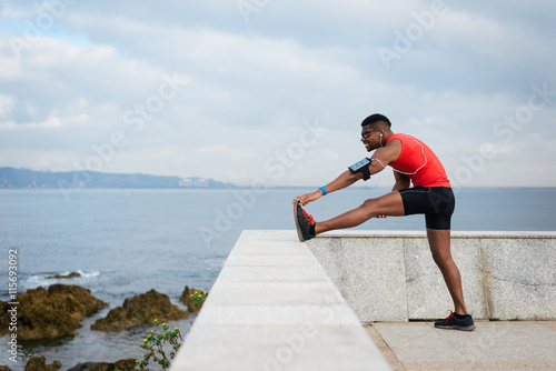 Male fit runner stretching towards the sea for warming up before running. Black athlete exercising.