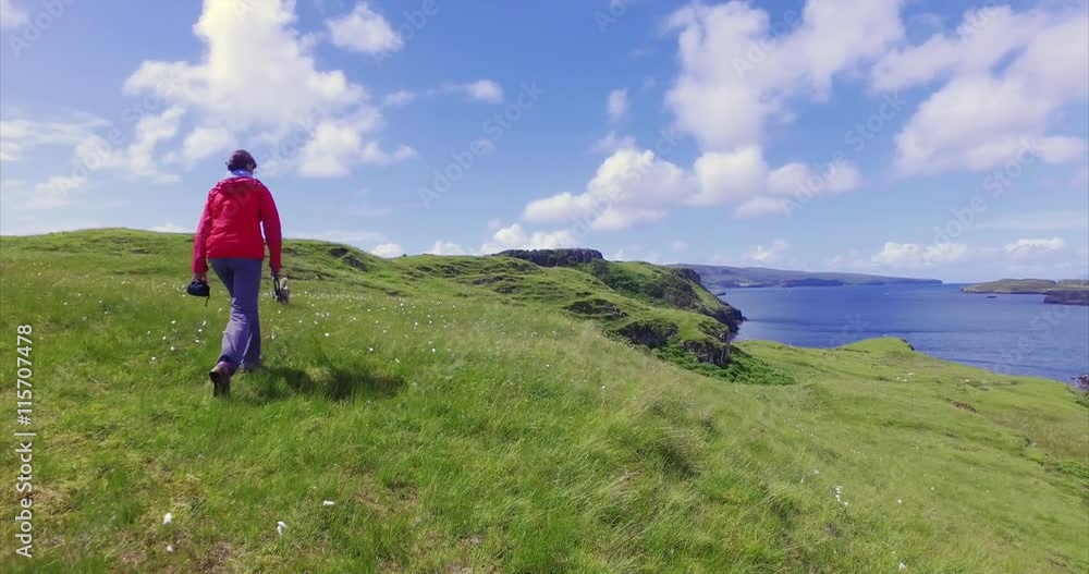 A female hiker walking through a sunny green meadow on the cost near Dunvegan on the Isle of Skye, Scottish Highlands.UK. A female hiker walking through a sunny green meadow on the cost near Dunvegan on the Isle of Skye, Scottish Highlands.UK.