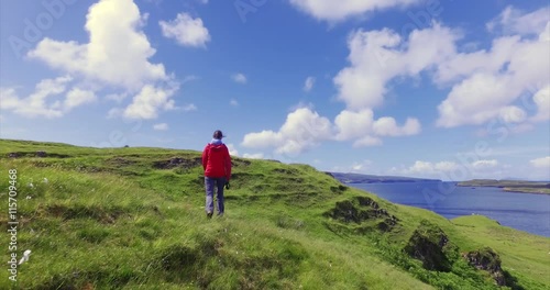 A female hiker walking through a sunny green meadow on the cost near Dunvegan on the Isle of Skye, Scottish Highlands.UK.