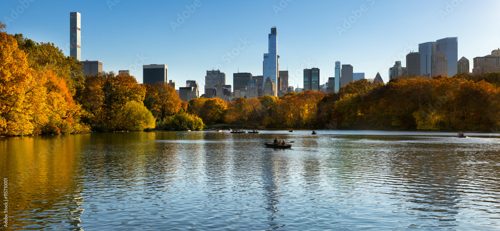 Fall in Central Park at The Lake with Midtown Manhattan skyscrapers. Panoramic afternoon cityscape view with colorful fall foliage. Manhattan, New York City