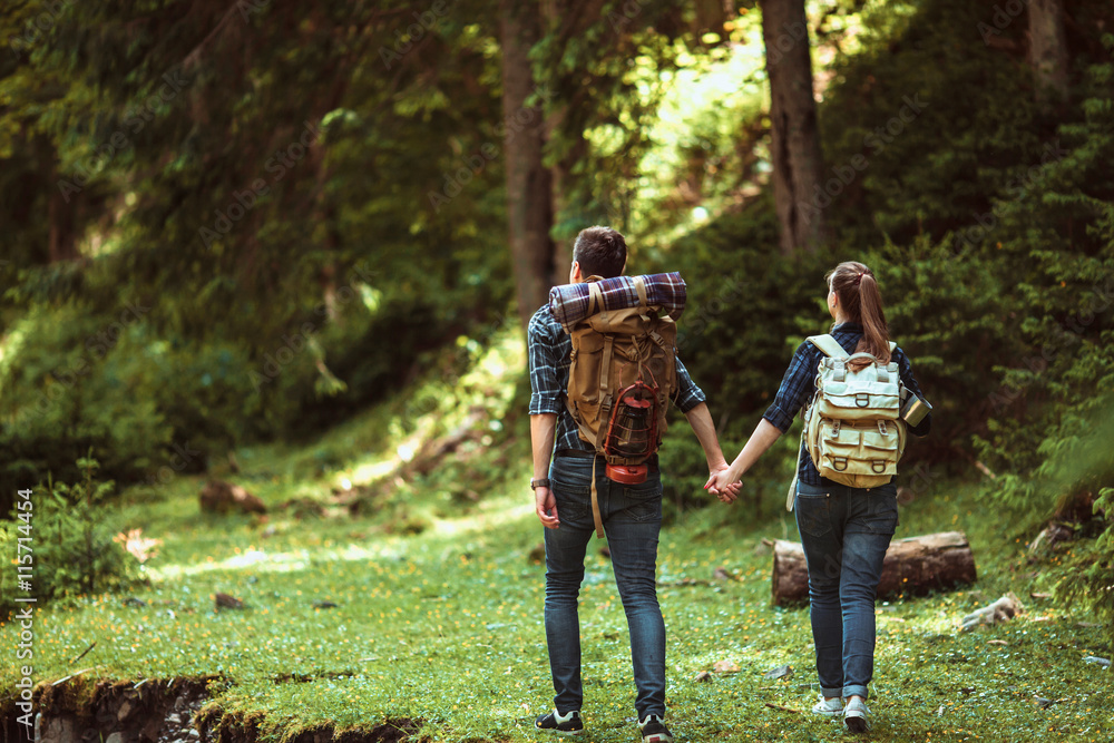 A couple hikers Hiking with backpacks walk along a beautiful mountain area holding hands . The concept of active rest