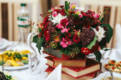 Rich autumn bouquet stands on a red books. Dinner table decorati