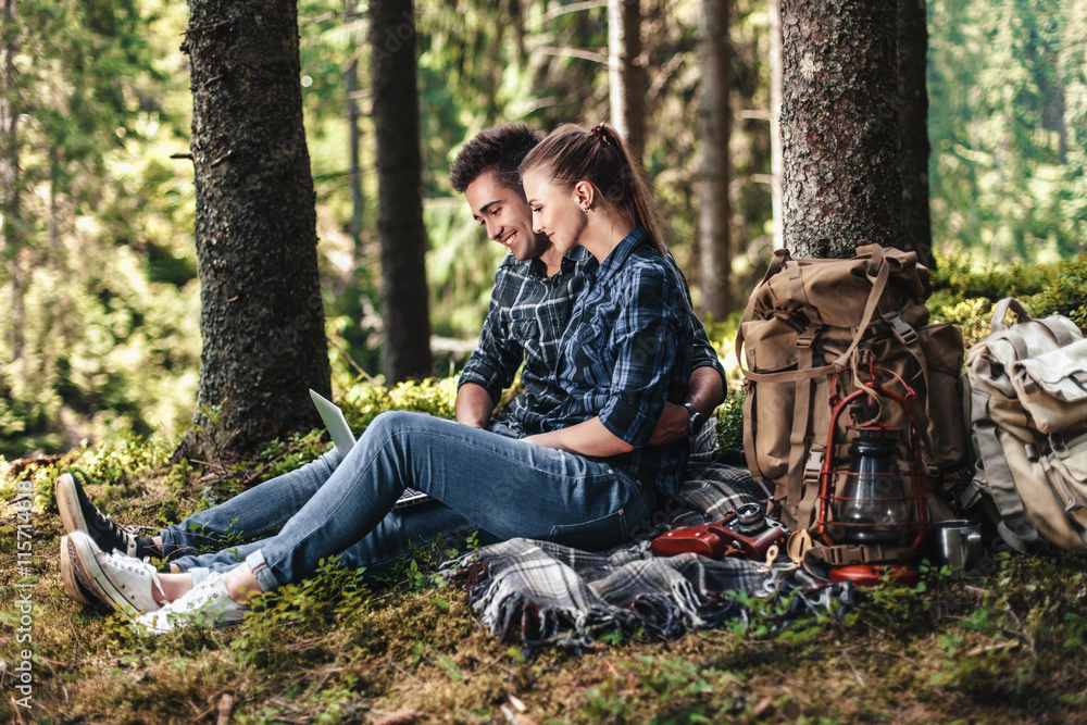 Obraz premium A couple of tourists sitting and looking at laptop in the woods. The concept of active rest