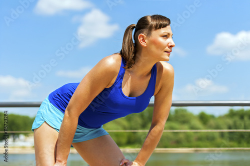 Fit jogger woman resting after run in city park by the river.