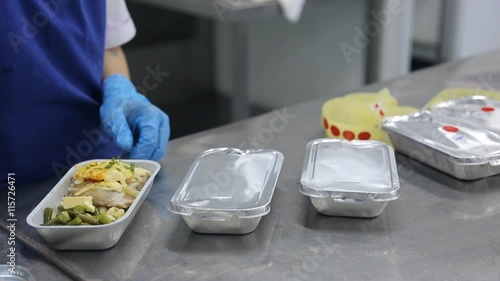 Packaging aluminum containers with food and labeling in factory of flight catering.