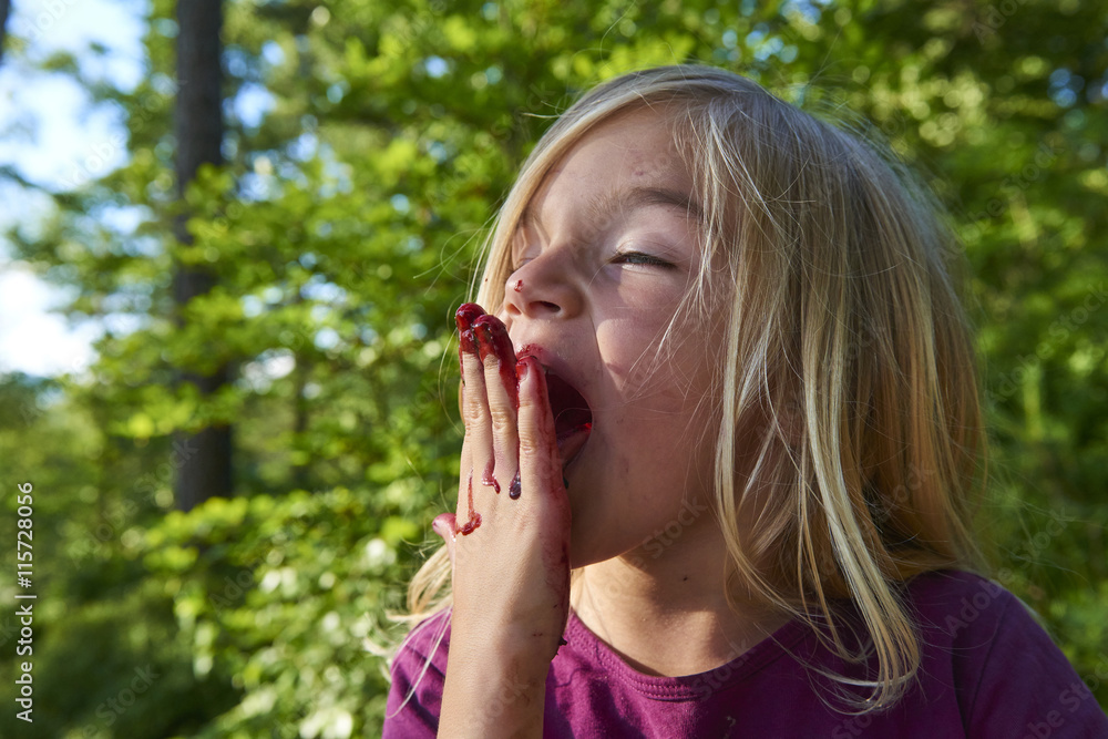 Child blond little girl picking fresh berries on blueberry field in forest. Child pick blue berry in the woods. Little girl playing outdoors. Hands red from crushed blueberries. Summer family fun. Child blond little girl picking fresh berries on blueberry field in forest. Child pick blue berry in the woods. Little girl playing outdoors. Hands red from crushed blueberries. Summer family fun.
