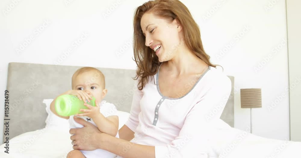 Smiling young mother feeding her baby girl her bottle Smiling young mother feeding her baby girl her bottle