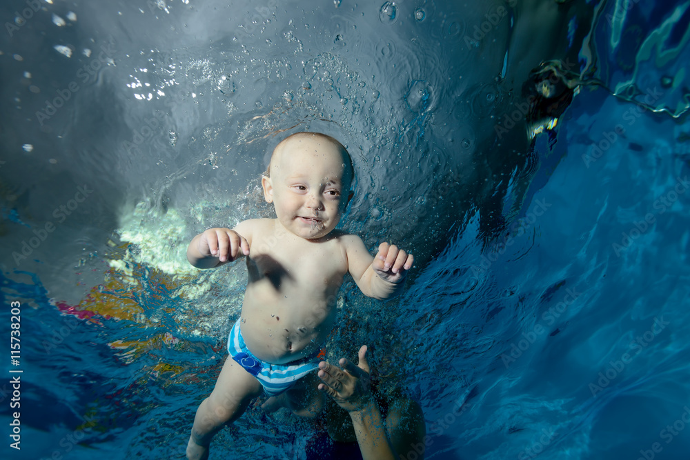 A baby swims underwater in the pool and smiling. Close-up. Portrait. Bottom view. Horizontal orientation