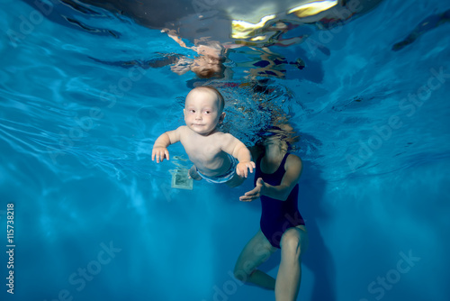 A little boy floats from my mother under the water in the pool on a blue background. Horizontal orientation