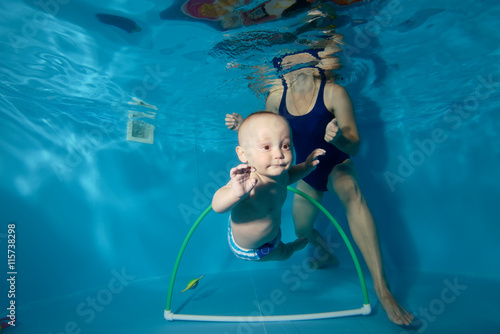 Happy baby trains with his mother underwater in the pool and swim through the Hoop. Portrait. Close-up. Horizontal orientation