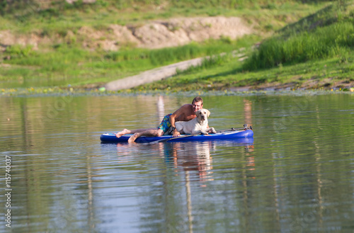 The dog and the man float by the boat on the lake.