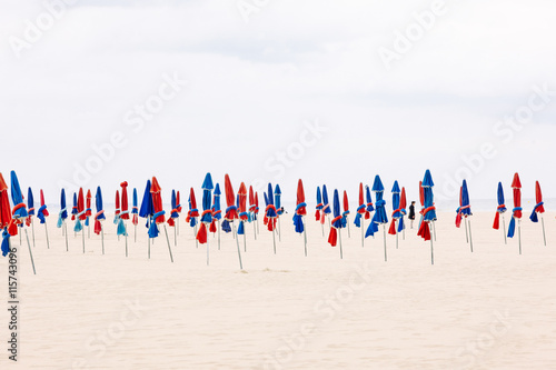 Man standing among closed parasols on beach (ID: 115743096)
