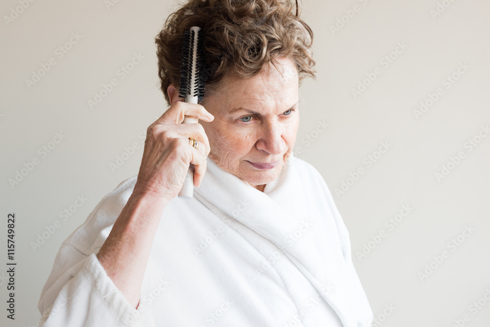 Head and shoulders view of older woman in white bathrobe brushing hair Head and shoulders view of older woman in white bathrobe brushing hair