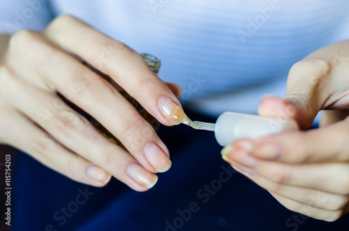 Woman with long fingers and nails applying transparent nail base at home  close up photo