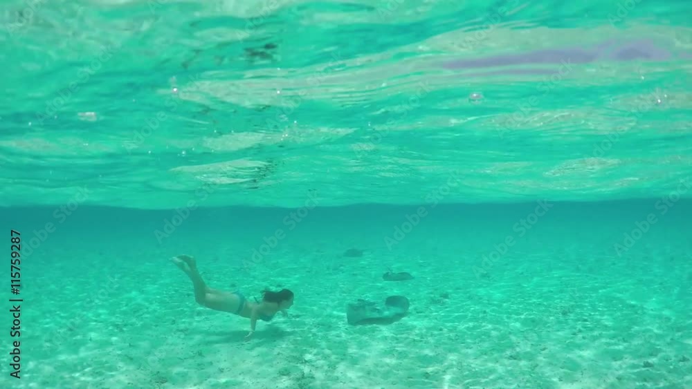 SLOW MOTION: Young woman swimming underwater with friendly stingray rays