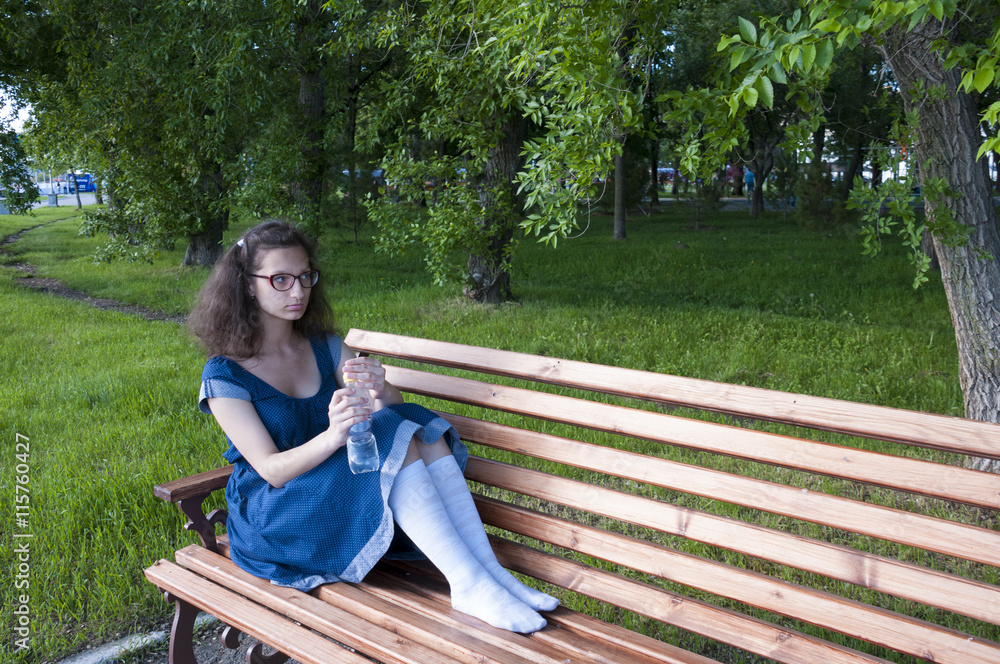 A girl sits on a park bench with a bottle of water A girl sits on a park bench with a bottle of water