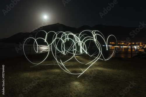 Light painting heart shapes over mountains, sea and night town background. Love. Night.