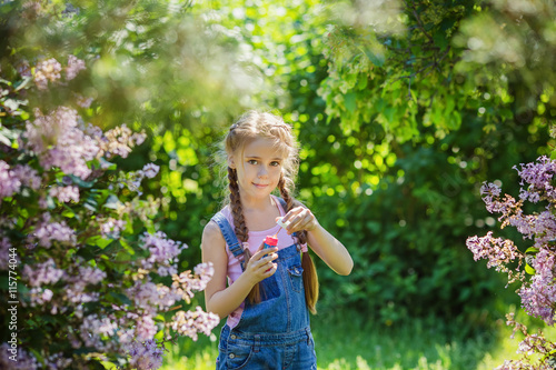 Portrait of beautiful little girl in lilac blossoming garden