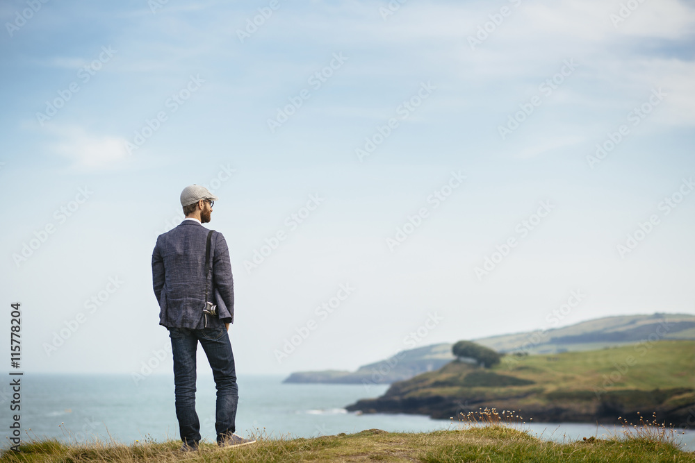 Rear view of man standing on grassy coast, looking at sea Rear view of man standing on grassy coast, looking at sea