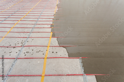 Electric floor heating system installation in new house. Closeup of concrete and red electrical wires photo