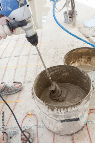 Electric floor heating system installation in new house. Worker use concrete hand mixer to prepare cement