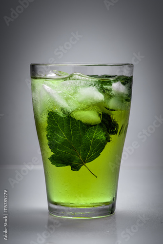 fresh cold drink with ice, mint leaves and black currant in glass on gray background