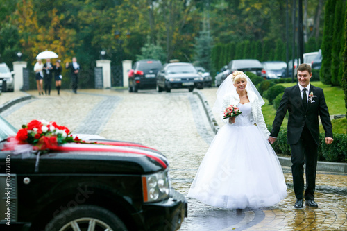 Fotografía Bride and groom go to the car holding their hands together