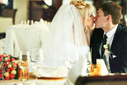 Bride and groom kiss sitting at the empty wedding table