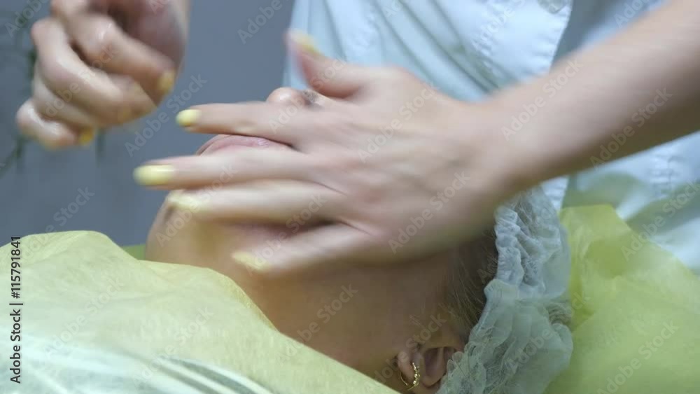 Beautician hands stroking the face of the client. Facial massage beautiful girl. Portrait of a young woman in the beauty salon. Cosmetologist doing massage of female face. Close-up. Beautician hands stroking the face of the client. Facial massage beautiful girl. Portrait of a young woman in the beauty salon. Cosmetologist doing massage of female face. Close-up.