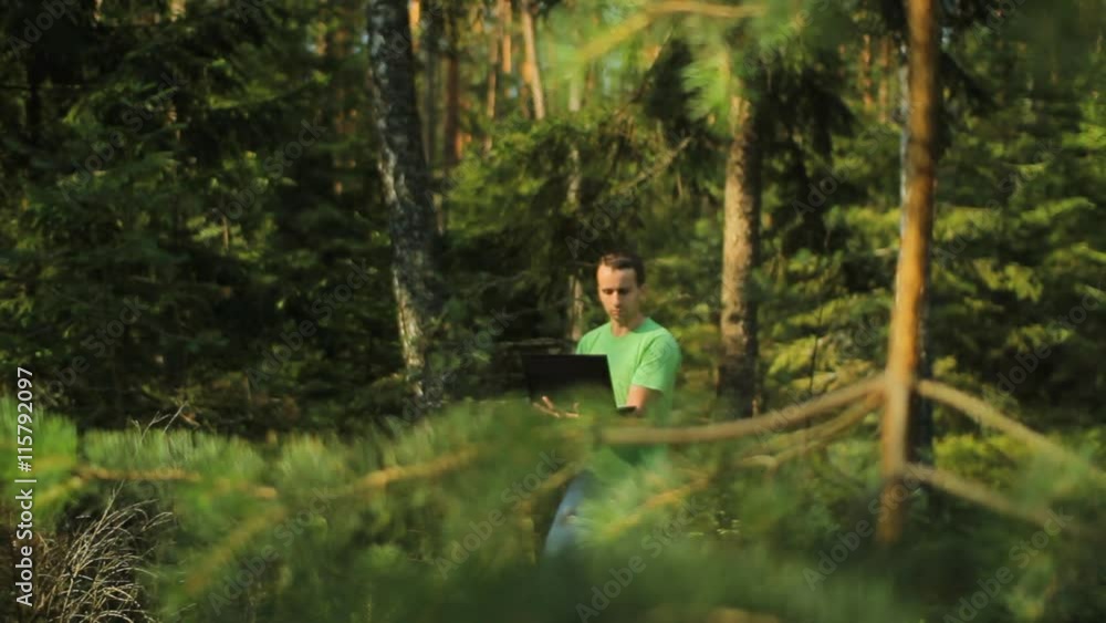 A man walks through the forest with a laptop and looking map He chooses the right direction A man walks through the forest with a laptop and looking map He chooses the right direction