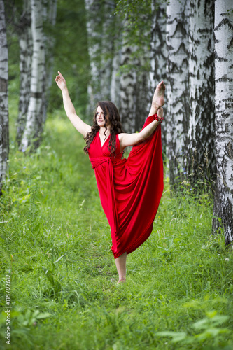 Beautiful young caucasian brunette woman in red dress outdoors, flexibility and stretching on nature