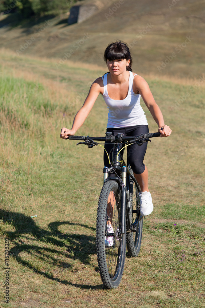 Fototapeta premium Young lady with bicycle on a spring meadow