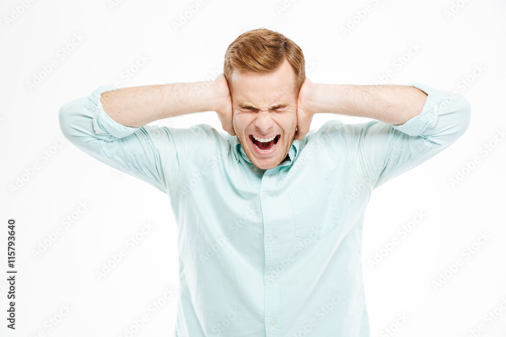 Irritated stressed young man covered ears by hands and shouting Irritated stressed young man covered ears by hands and shouting