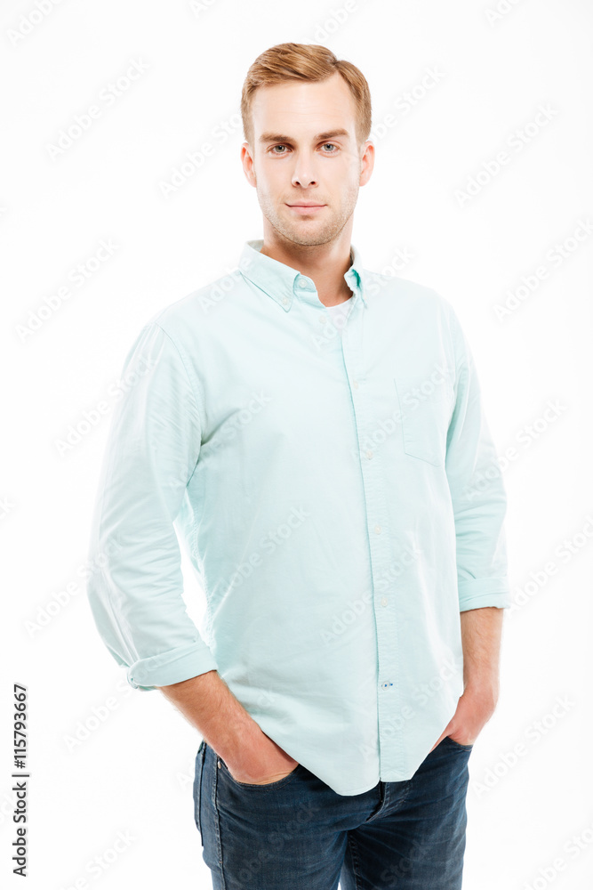 Serious attractive young man standing with hands in pockets Serious attractive young man standing with hands in pockets