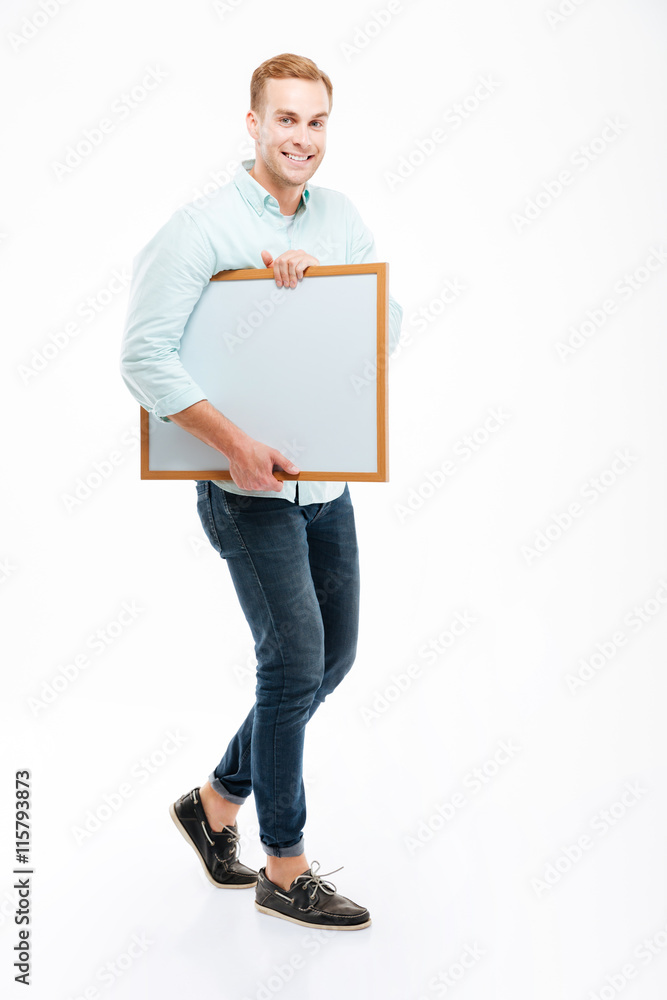 Full length of cheerful young man walking and holding whiteboard Full length of cheerful young man walking and holding whiteboard