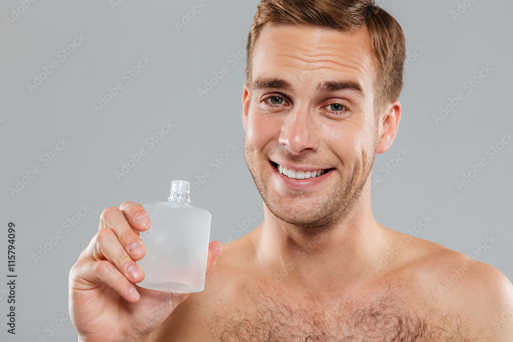 Smiling young man applying lotion after shave on face Smiling young man applying lotion after shave on face