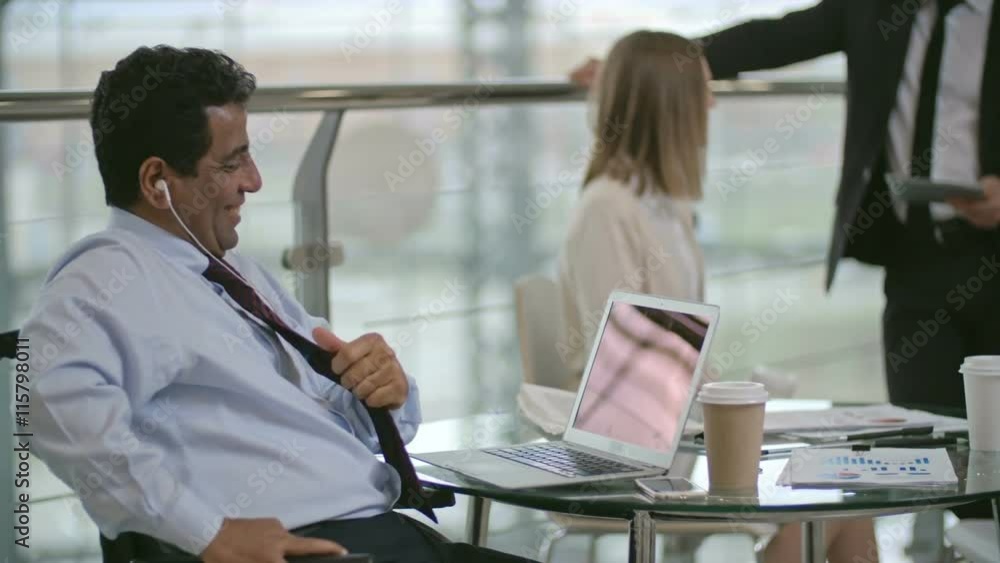 Laughing businessman sitting on wheelchair and talking with somebody on laptop Laughing businessman sitting on wheelchair and talking with somebody on laptop